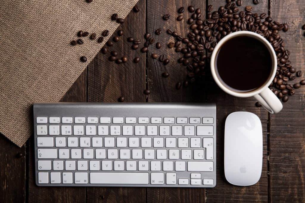 A keyboard, mouse and coffe mug on a table.